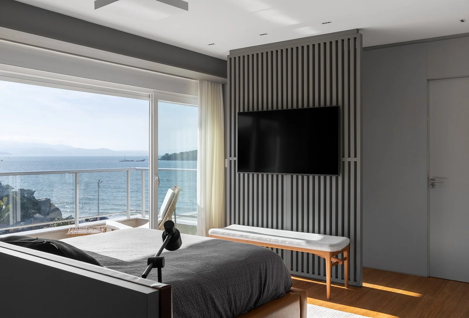 Dormitório com painel ripado de TV e vista para o mar — Cobertura Bleu, VK Arquitetos